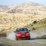 Czerwony rajdowy samochód pędzi w tumanach kurzu po pustynnym odcinku