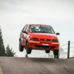 Czerwony samochód rajdowy wyskakujący nad wzniesieniem na wiejskiej drodze