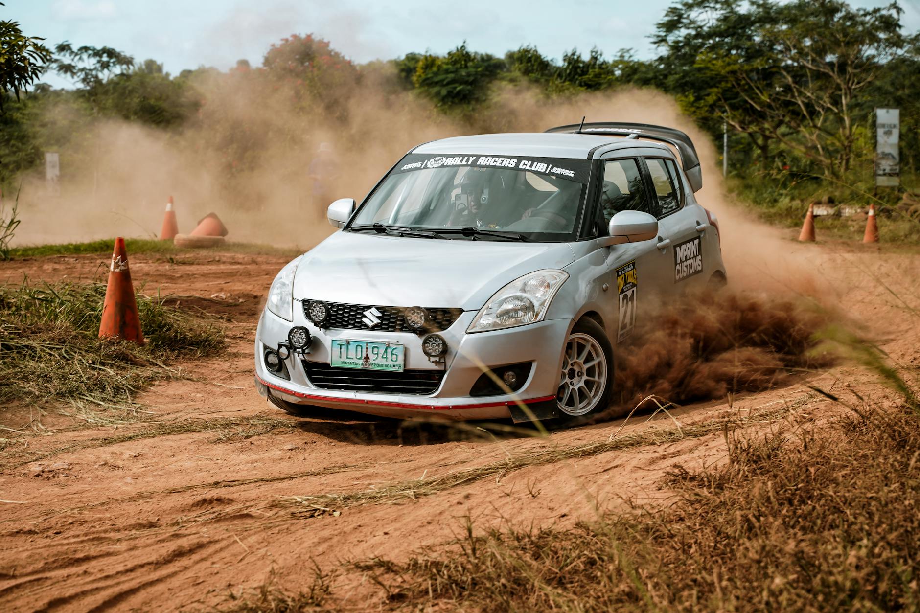 Srebrne auto rajdowe pędzi po szutrowej trasie w tumanach kurzu