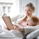 Mama z córką czytające razem książkę w łóżku