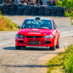 Czerwony samochód rajdowy WRC na trasie w Ritsonie, kibice w tle