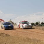 Dwa samochody rajdowe WRC pędzą po szutrowej trasie w tumanach kurzu
