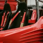 Wnętrze czerwonego buggy z czarnymi fotelami i pasami szelkowymi